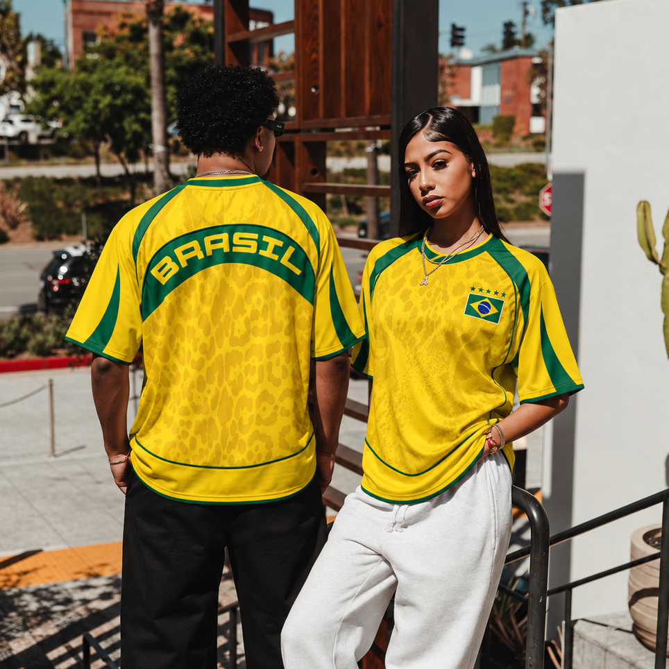 Two models wearing Varldens yellow and green Brazil soccer jerseys, standing on outdoor steps. The model on the left shows the back of the jersey with 'BRASIL' printed in green, while the model on the right shows the front with the Brazilian flag crest.