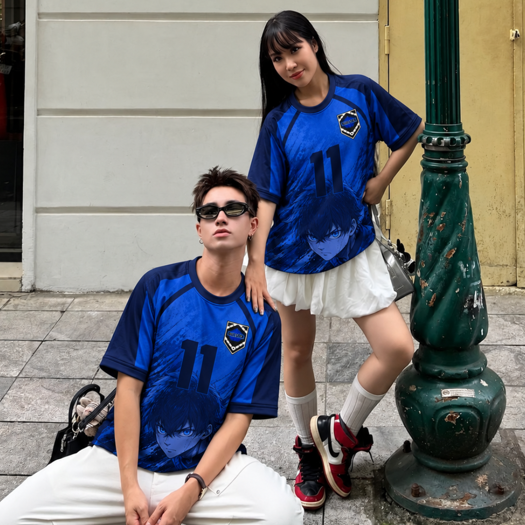 Two models wearing Varldens matching blue and black graphic t-shirts with the number 11, posing outdoors next to a green street lamp. Blue Lock jersey with Isagi pattern.
